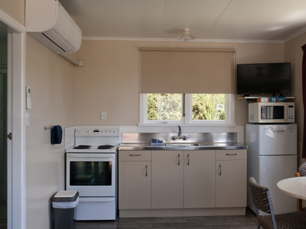 Kitchen with oven in view, microwave on top of fridge and TV mounted above that